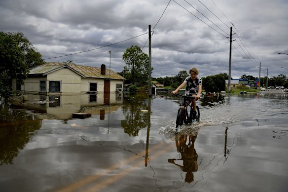 A boy rides a bike throught the flood water at Wilberforce on the Hawkesbury River on Wednesday.