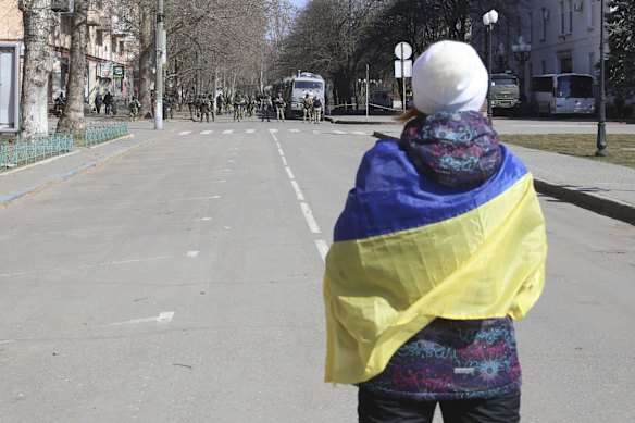 A woman wearing a Ukrainian flag stares at Russian troops during a rally against Russian occupation in Kherson.
