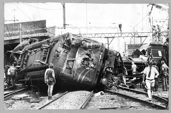 The battered engine of the train lies on its side across the rails, behind it is the wreckage of one of the carriages, January 19, 1977.