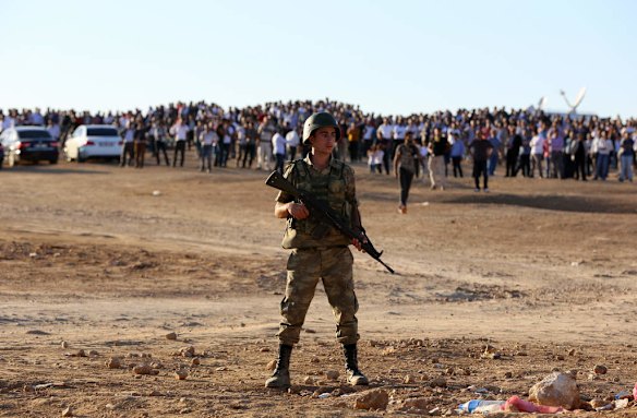 A soldier helps secure the area as Turkish Kurds gather near the border with Syria to watch as mortar shells land in the distance as fighting intensified between Syrian Kurds and the militants of the Islamic State group in nearby Kobani in Syria, from their vantage point near Suruc, Turkey, Saturday, Oct. 4, 2014.  Photo by AP