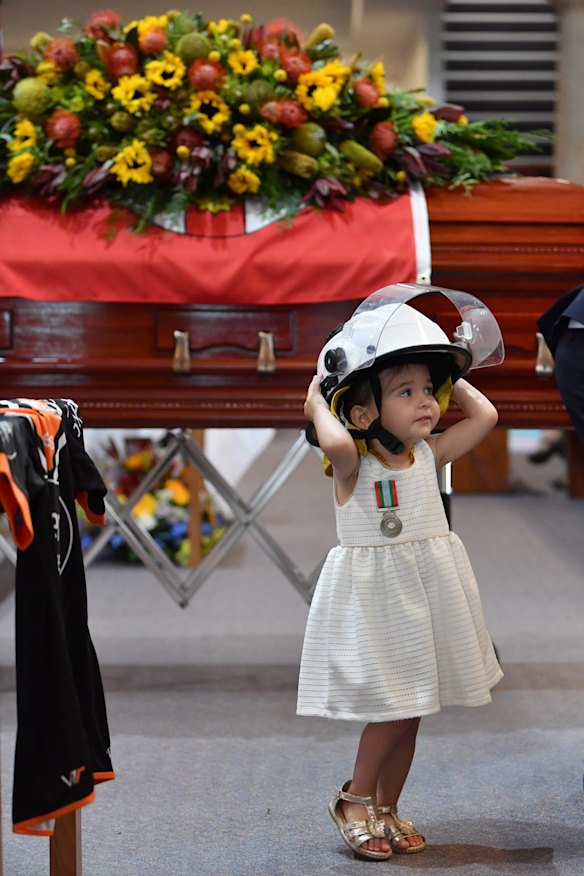 Charlotte O'Dwyer, the young daughter of Rural Fire Service volunteer Andrew O'Dwyer stands in front of her fathers casket wearing his helmut after being presented with her fathers service medal by RFS Commissioner Shane Fitzsimmons.