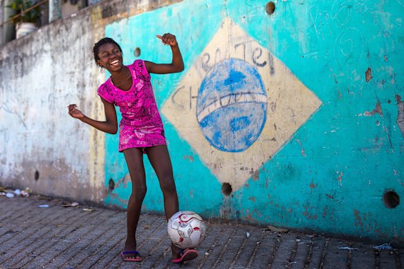 A girl poses while playing football in the Chacara do Ceu favela.