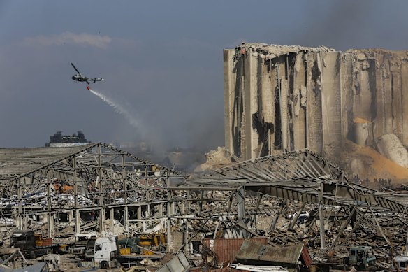 A helicopter drops water on smoldering buildings in the city's port, destroyed by an explosion a day earlier.