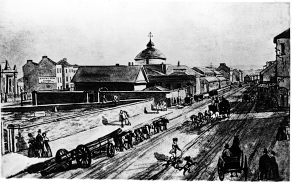 Scene of George Street looking north in 1842. On the left behind the wall is the old burial ground which is now Sydney Town Hall.