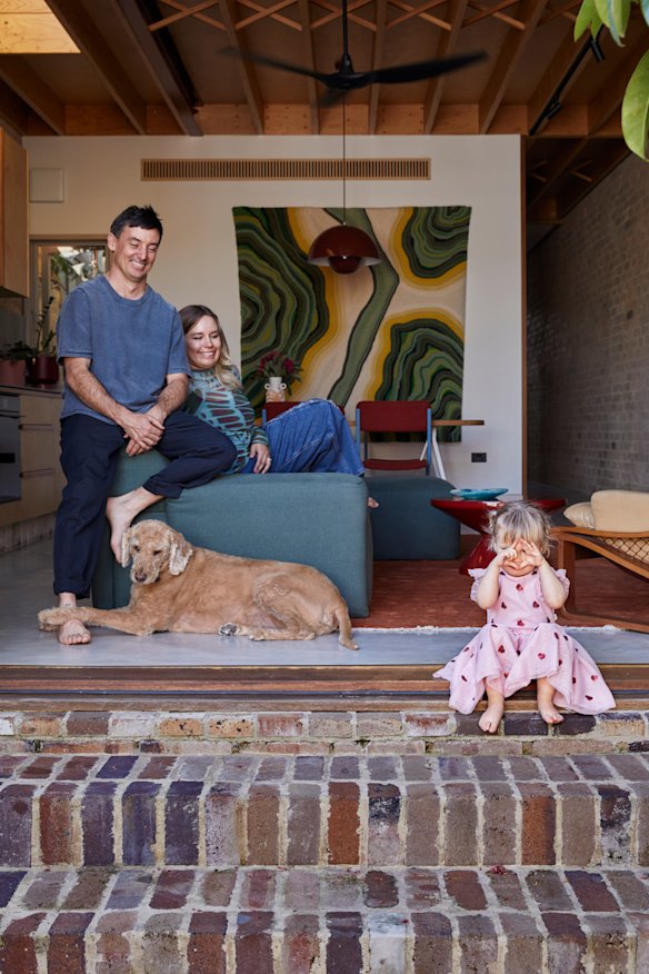 In the home’s living/kitchen/dining room, Tom Hume and Joscelyn Tarr watch as daughter Ronnie sits on recycled bricks and Otis relaxes.