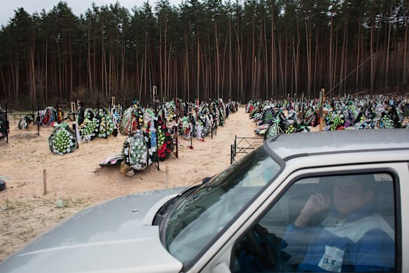 A cemetery worker waits in a car for a funeral at a cemetery in Bucha.