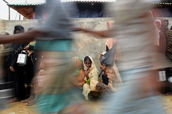 Rohingya refugee women wait in their line as the men in their line run past for a meal.