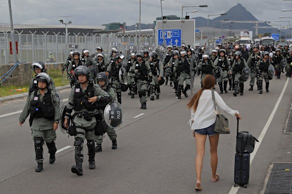 A passenger walks pass riot polices as protestors blocked a road outside the airport in Hong Kong, Sunday, Sept .1, 2019. 