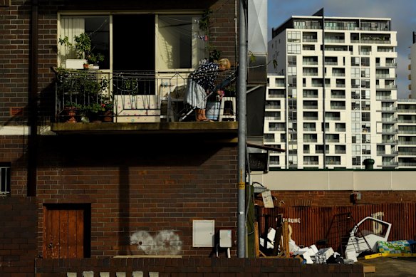 An elderly woman waters plants on her balcony. 