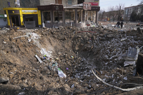 People walk past a crater from an explosion in Mariupol.