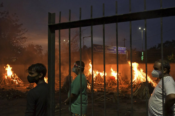 People watch burning funeral pyres of their relatives who died of COVID-19 in a ground that has been converted into a crematorium in New Delhi.