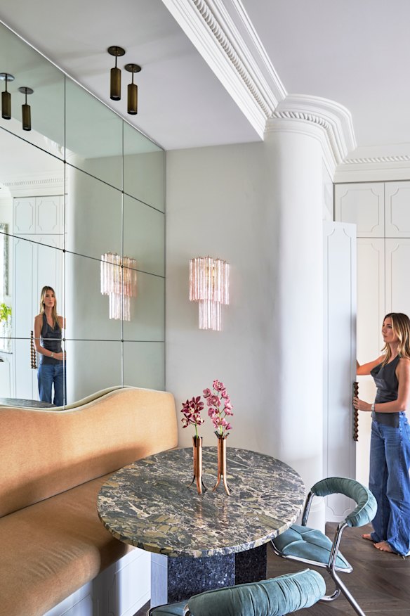 A mirrored wall adds a sophisticated mood to the dining space. It features a built-in banquette sofa, marble table, mid-century chairs and Murano glass sconce.