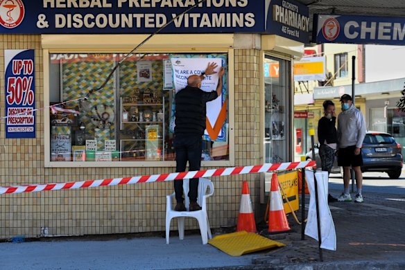 A man puts up a sign informing the public the pharmacy is a COVID-19 vaccination site in Bexley, in the Bayside LGA which is under additional restrictions.