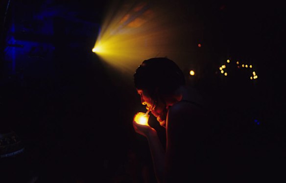 A girl lights a cigarette with a candle at a Psychadelic Party at The Northwood Garage, Newtown.