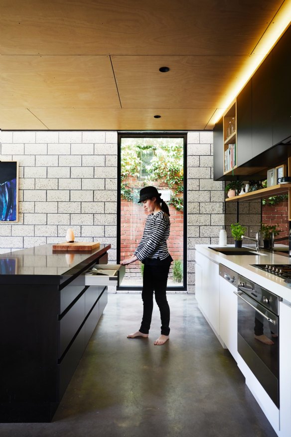 Harriet in the kitchen, where a warm, panelled plywood ceiling softens theindustrial look of the polished concrete floor and honed brick wall.
