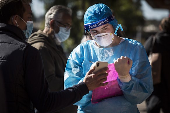 A woman in full PPE takes down details as people queue along Ninth Street in Campsie to get tested at a Covid Testing Clinic. Campsie in South West Sydney is one of the Sydney hotspots.
