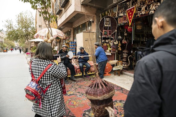 A woman uses her smartphone to take photographs as musicians perform with their instruments at a store in the Old City in Kashgar, Xinjiang autonomous region, China.