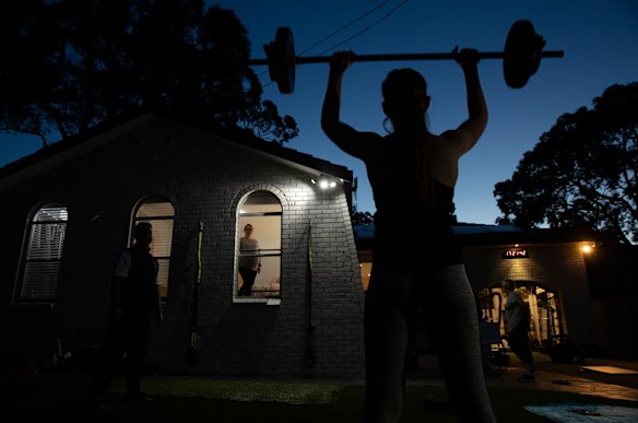 Fitness trainer, Chris Thomas, conducts training sessions in his front yard. His eight-month pregnant wife, Michelle, watches safely from the window.