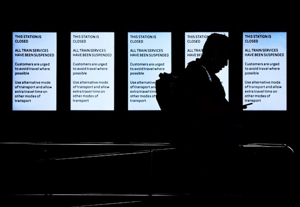 Commuters at Central Station stand in-front of the departures board displaying a notice that all train services are suspended.