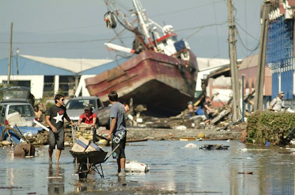 Residents gather their belongings near a fishing boat washed up by a wave generated by an earthquake in Talcahuano Port, a city just outside Concepcion.
