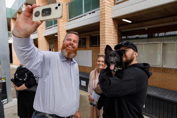 Labor candidate Dan Repacholi takes a selfie with voters Hannah Berthold and Cody Legg and their puppy Odin in the voting queue at Singleton Heights polling centre in the upper Hunter Valley town of Singleton.