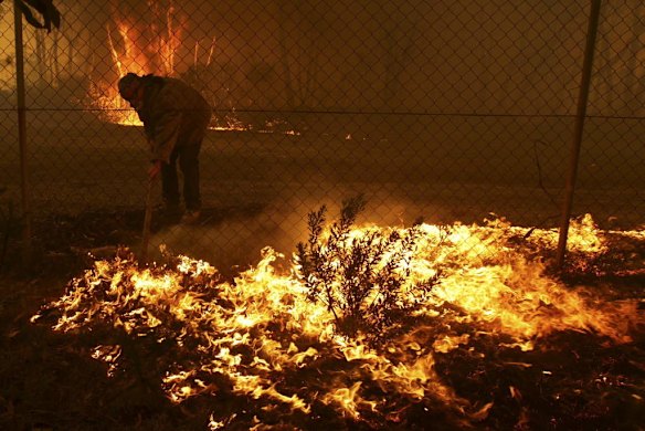 A resident protects his property as an out of control bushfire threatens four homes near Newnes train station.