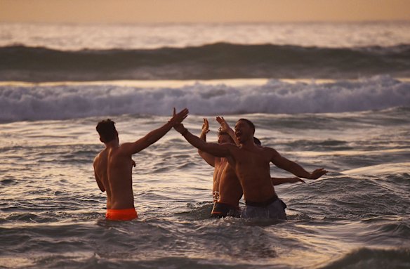 A group of men celebrate as the sun rises over Bondi Beach/