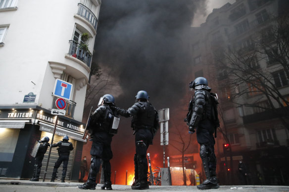 Riot police officers take position as a shopfront nearby burns. 