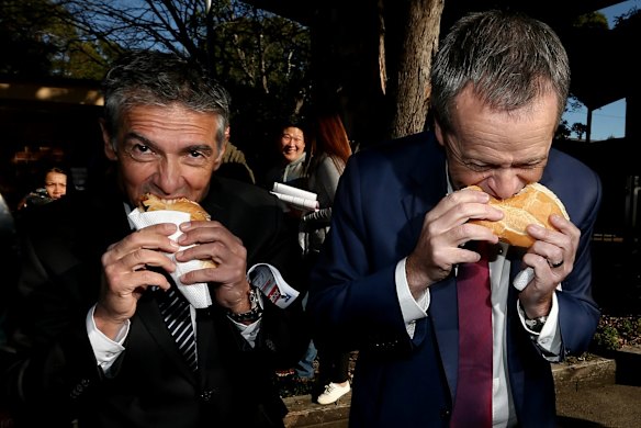 Opposition Leader Bill Shorten eats a sausage in a roll with onion and tomato sauce, together with ALP candidate for Reid, Angelo Tsirekas, during a visit to the polling booth at Strathfield North Public School in the seat of Reid.
