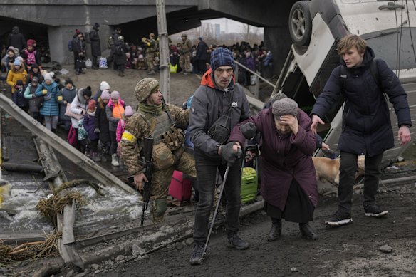 An elderly lady is assisted while crossing the Irpin river, under a bridge that was destroyed by a Russian air strike, as civilians flee the town of Irpin, Ukraine.