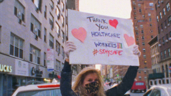 A New Yorker holds up a sign thanking the city’s frontline workers in <i>Epicenters</i>.