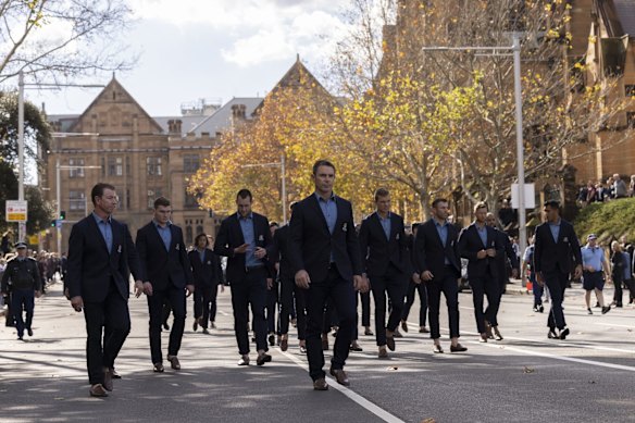 Players and coaches from the current NSW Blues team, led by Coach Brad Fittler, walk behind the hearse.