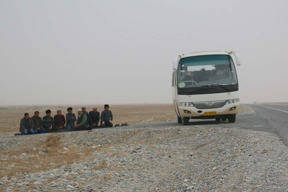Uighur men stop their bus on the roadside to pray, on a highway leading into Hotan.