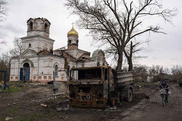 A woman rides by a burnt vehicle in front of a damaged church in Lukashivka, near the city of Chernihiv. Residents say Russian soldiers used the house of worship for storing ammunition, and Ukrainian forces shelled the building to make the Russians leave.