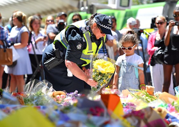 A policewoman and child contribute to floral tributes.
