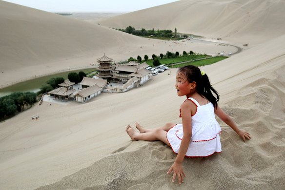 A girl sits atop the Singing Dunes of Crescent Lake, near Dunhuang. Photo: Getty Images/Feng Li.