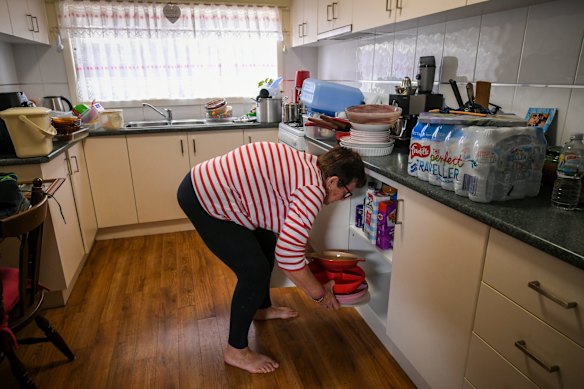 Glenys removes kitchen containers from the bottom cupboards.