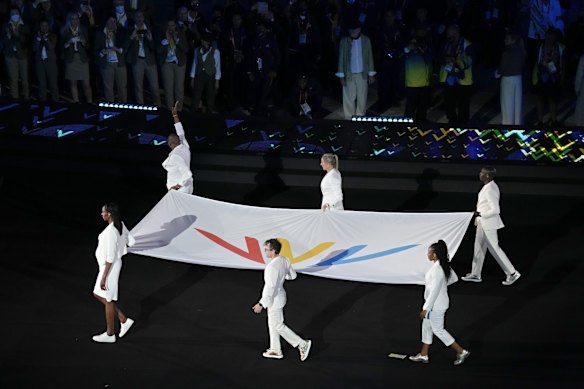 The Commonwealth Games flag is carried past the athletes.