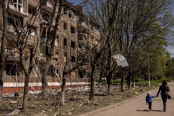 A woman and her child walk past a residential apartment block damaged by a Russian missile strike in Kramatorsk.