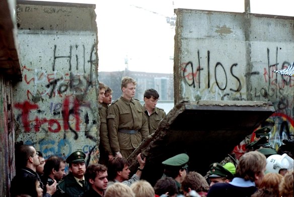 East German border guards look through a hole in the Berlin Wall after demonstrators pulled down the segment on November 11, 1989.