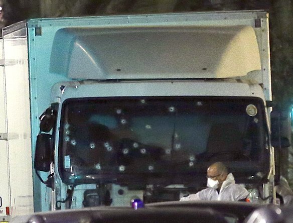A forensic officer stands near a van with its windscreen riddled with bullets.