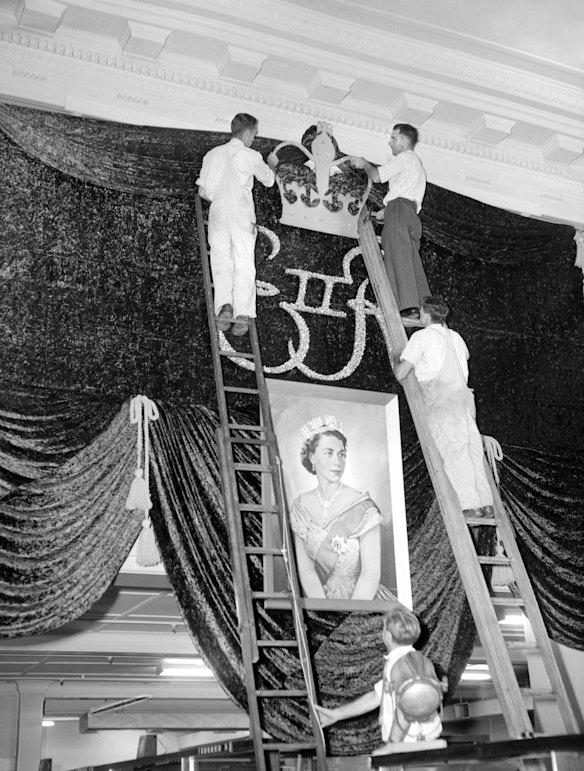 Time is running out but hundreds of workers are still engaged making Melbourne a city of colour and beauty for the Queen. This scene is at the Commonwealth Bank in Collins Street, Melbourne, Victoria, being adored with decorations for the royal visit in February 1954.