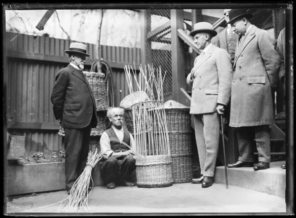 Sir Dudley de Chair (2nd from right) watches a man weaving a large cane basket at the Blind Institute, Sydney, 8 July 1925.