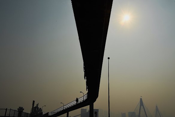 A smoke haze fills the sky as cyclists and pedestrians make their way along the overpass over the Anzac Bridge in Rozelle.