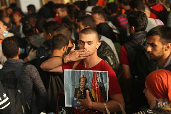 A migrant from Syria holds a picture of German Chancellor Angela Merkel as he and approximately 800 others arrive from Hungary at Munich Hauptbahnhof main railway station in Munich, Germany. 