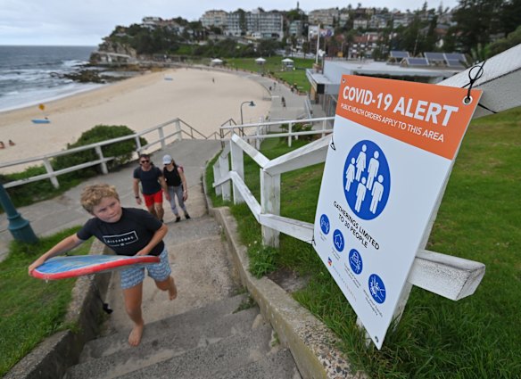 Beachgoers walk past a COVID-19 alert sign on New Years Eve at Bronte Beach in Sydney.