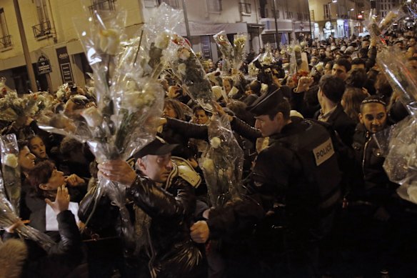 People hold bouquet of flowers as  a French police officer tries to maintain the mob during a demonstration outside a kosher grocery store where four hostages were killed on Friday in Paris, Saturday, Jan. 10, 2015. Hundreds of thousands of people marched Saturday in cities from Toulouse in the south to Rennes in the west to honor the victims, and Paris expects hundreds of thousands more at Sunday's unity rally. More than 2,000 police are being deployed, in addition to thousands already guarding synagogues, mosques, schools and other sites around France.