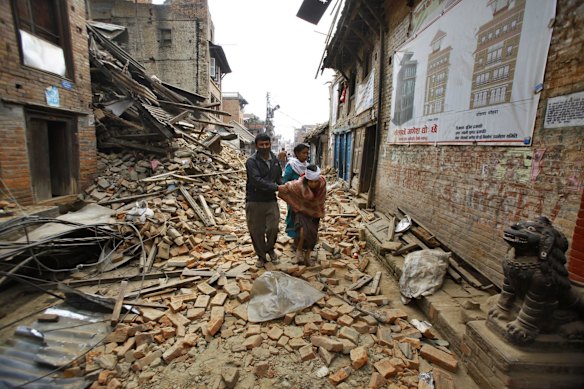 An elderly injured woman is taken home through earthquake debris after treatment in Bhaktapur near Kathmandu, Nepal, Sunday, April 26, 2015.