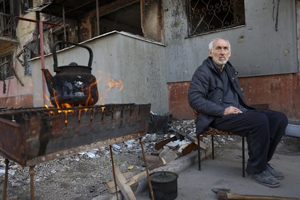 A local man sits in front of an apartment building damaged from heavy fighting as he waits for the kettle to boil in an area controlled by Russian-backed separatist forces in Mariupol.