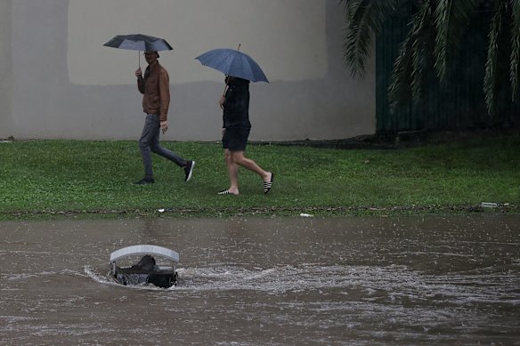People walk past a partially submerged garbage bin in the rising Parramatta River.